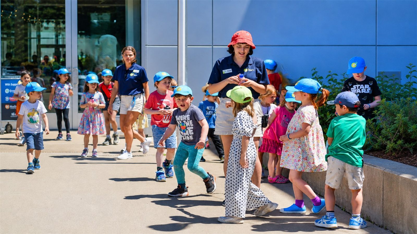 Grupo de crianças com bonés do Discovery Centre acompanhadas por educadoras em atividade ao ar livre
