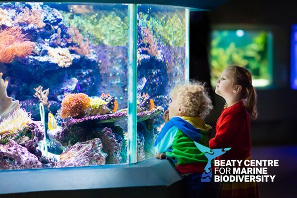 Duas crianças observando um grande aquário de recife de corais no Beaty Centre for Marine Biodiversity